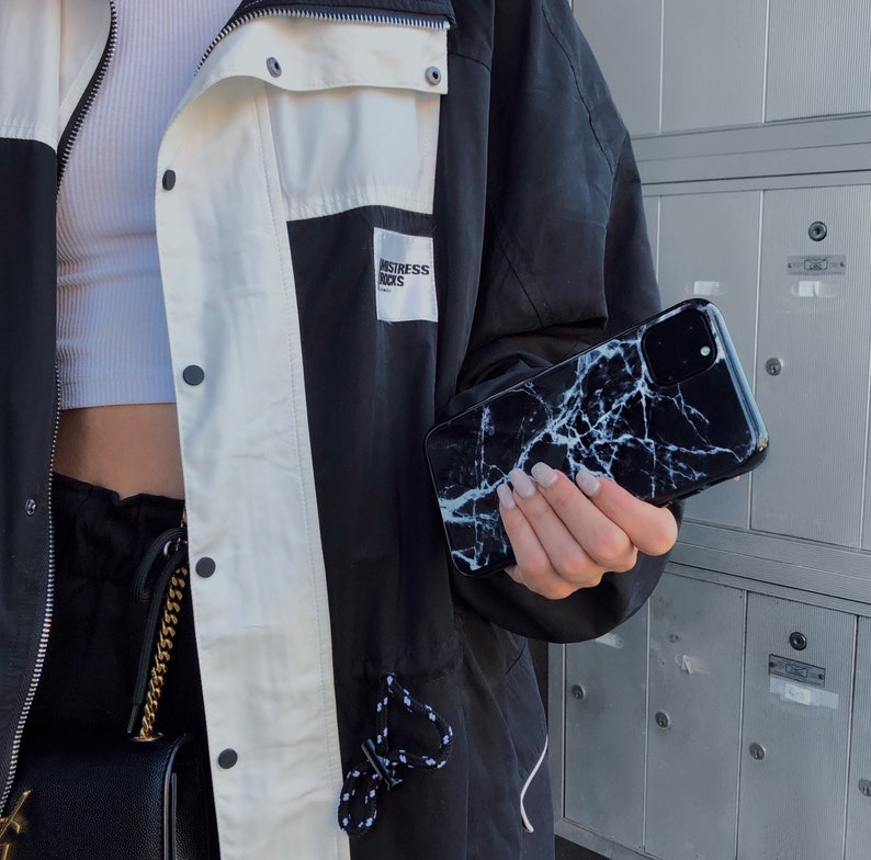 May include: A black and white marble phone case with a white and black jacket. The jacket has a white patch with the text "Distress Kicks" on it.