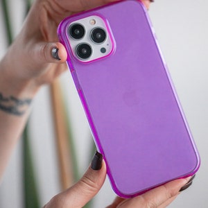 May include: A clear purple phone case with a raised camera bump and a white Apple logo.