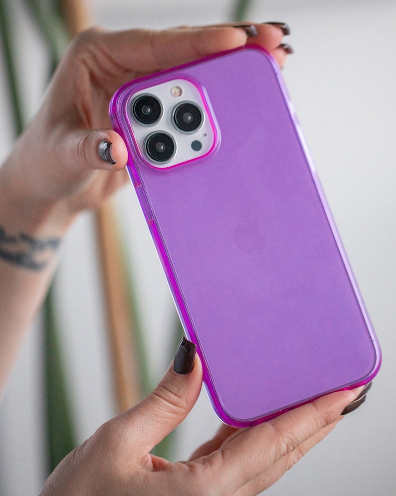 May include: A clear purple phone case with a raised camera bump and a white Apple logo.
