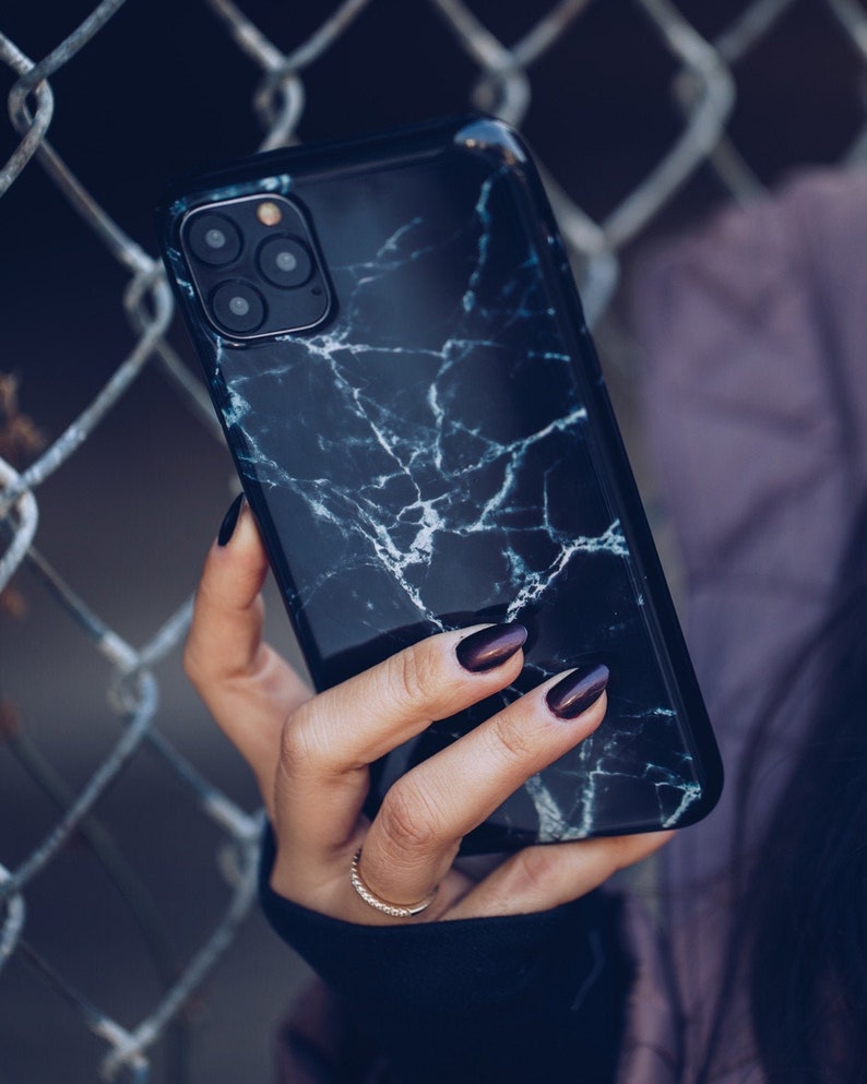 May include: A black phone case with a white marble pattern. The case has a camera lens cutout and a black border.