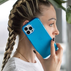 May include: A bright blue smartphone case with a clear border. The phone case is held up to the ear. The phone has three camera lenses. The person is wearing a white shirt and has a braided hairstyle.
