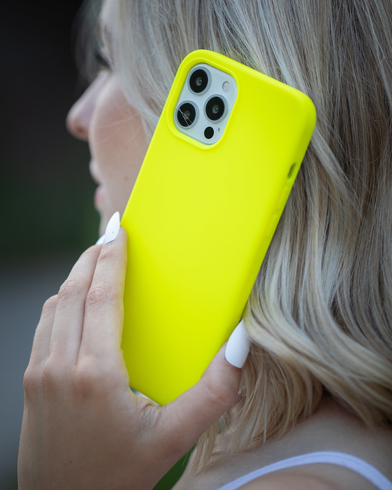 May include: A bright yellow phone case with a black camera lens and a white border. The case is held in a person's hand.