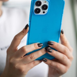 May include: A bright blue phone case with a clear border, held in hands. The case covers a phone with three camera lenses. The phone case is a vibrant, solid color, and the clear border adds a sleek design element.