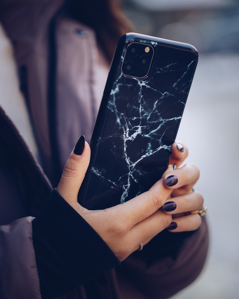 May include: A black phone case with a white marble pattern. The case has a triple camera lens on the back.