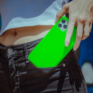 K&ouml;nnte beinhalten: Eine leuchtend gr&uuml;ne Handyh&uuml;lle mit einem Ausschnitt f&uuml;r das Kameraobjektiv. Die H&uuml;lle befindet sich in der Ges&auml;&szlig;tasche einer Person.