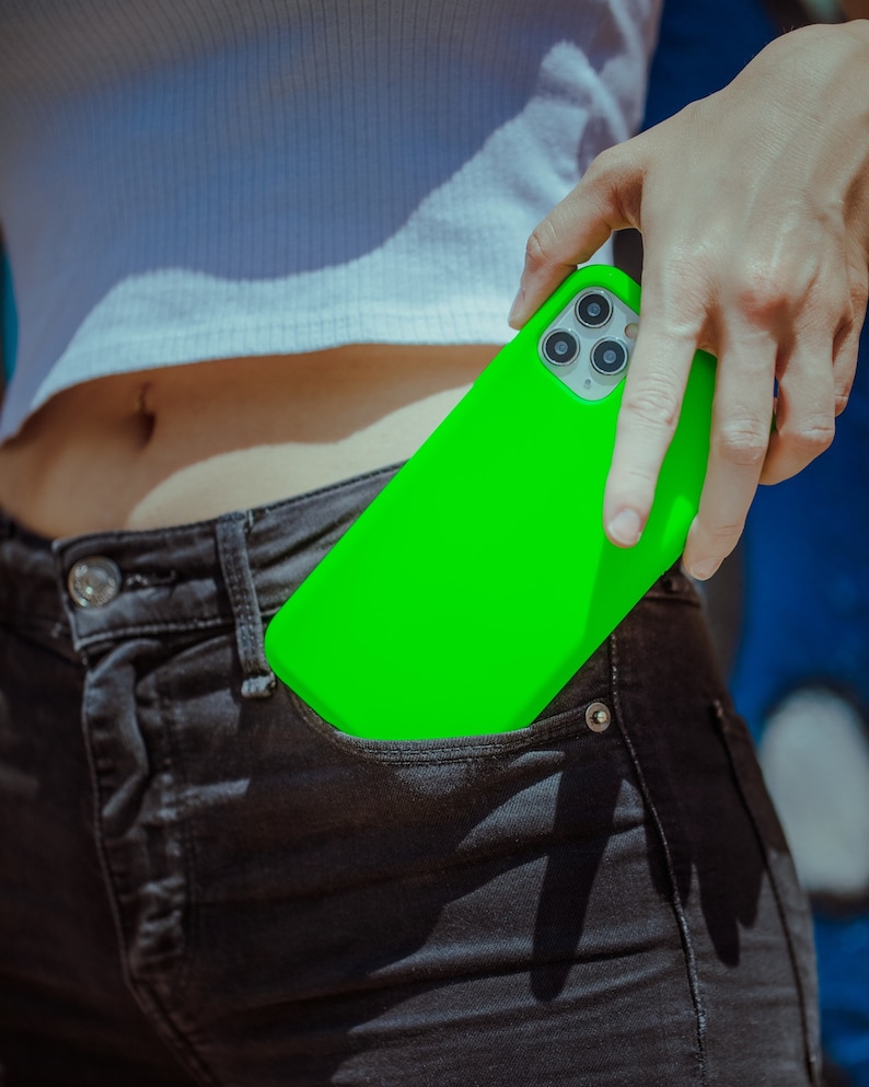 K&ouml;nnte beinhalten: Eine leuchtend gr&uuml;ne Handyh&uuml;lle mit einem Ausschnitt f&uuml;r das Kameraobjektiv. Die H&uuml;lle befindet sich in der Ges&auml;&szlig;tasche einer Person.