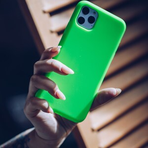 K&ouml;nnte beinhalten: Eine leuchtend gr&uuml;ne Handyh&uuml;lle mit einem schwarzen Kameraobjektiv. Die H&uuml;lle ist aus weichem, flexiblem Material.