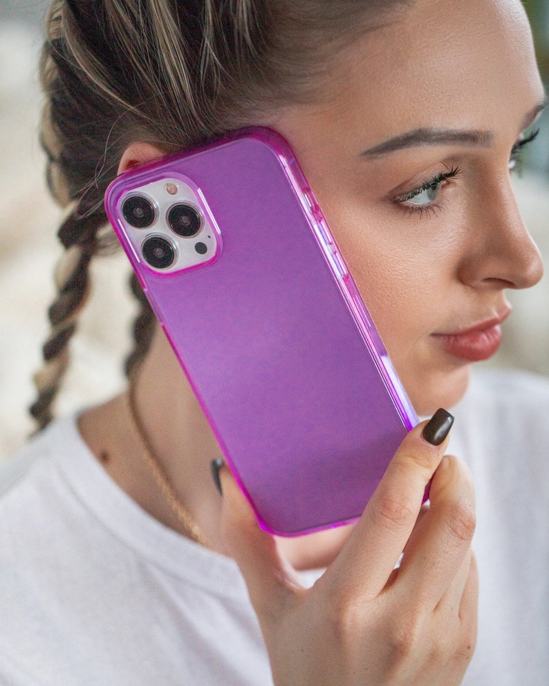 May include: A purple phone case with a clear back and a raised camera bump. The case is made of a flexible material and has a smooth finish.