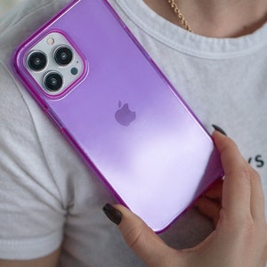 May include: A purple iPhone case with a clear back and a raised camera bump. The case has a subtle shimmer and a pink outline.