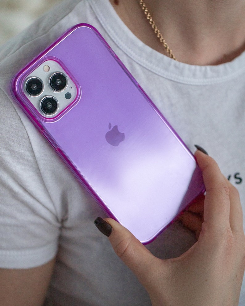 May include: A purple iPhone case with a clear back and a raised camera bump. The case has a subtle shimmer and a pink outline.