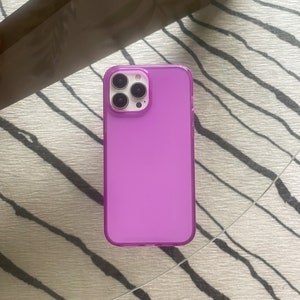 May include: A clear purple phone case with a raised camera bump. The case is made of a flexible material and has a smooth finish.