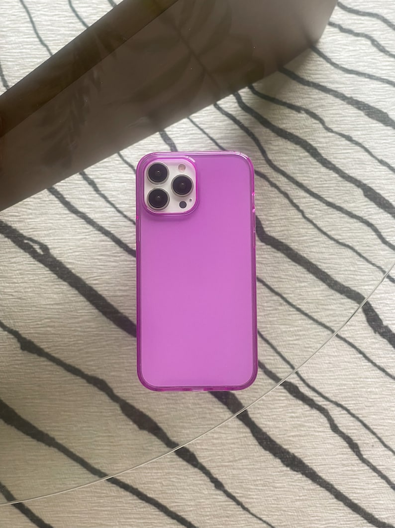 May include: A clear purple phone case with a raised camera bump. The case is made of a flexible material and has a smooth finish.