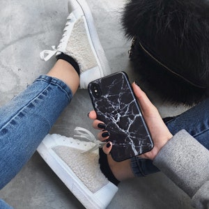 May include: A black and white marble phone case with a white background. The case is on a person's hand, and the person is wearing blue jeans and a white sweater.
