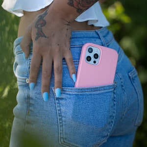 May include: A pink phone case with a camera lens cutout is in the back pocket of blue jeans.