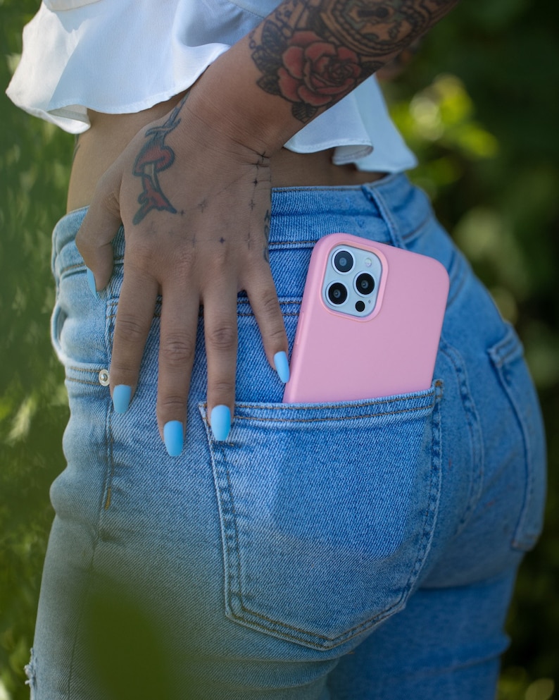 May include: A pink phone case with a camera lens cutout is in the back pocket of blue jeans.