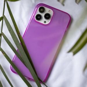 May include: A purple phone case with a clear back and a pink border. The case has a camera lens cutout with three black circles.