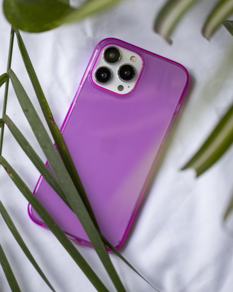 May include: A purple phone case with a clear back and a pink border. The case has a camera lens cutout with three black circles.
