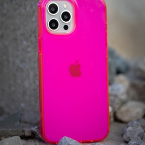 May include: A bright pink phone case with a clear back and a raised camera bump. The case has a white Apple logo on the back.