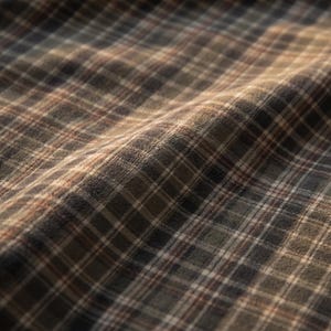 May include: A soft, textured fabric featuring a classic plaid pattern in shades of dark olive green, muted brown, and charcoal gray, accented by thin, intersecting white and light orange lines that create a grid across the surface.