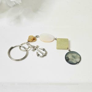 May include: A silver keychain with an anchor charm, a small seashell, and various light-colored, irregularly shaped beads. The keychain is designed with a nautical theme.