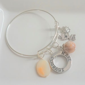 May include: Silver charm bracelet with a variety of charms, including a sun, the word "LOVE", a round charm with the words "HAVE COURAGE", and a peach-colored stone.