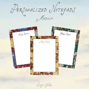 May include: Three medium rectangular notepads with white centers and marbled borders in red, blue, brown, and green. Each notepad features the printed name Margo Brooks at the top. The text Personalized Notepads Medium and Siggy Haus is visible.