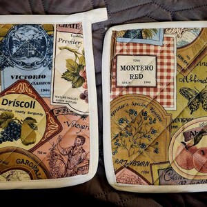 May include: Two white quilted pot holders with a patchwork design featuring various wine labels and images of grapes, butterflies, and a peacock. The labels include names like "Monterro Red", "Milenti Vineyard", "Driscoll", and "Abbottier".