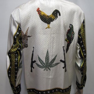 Op de afbeelding: Wit overhemd met gouden stippen en zwart-gouden sierlijsten. De achterkant heeft geborduurde afbeeldingen van een haan, een papegaai, een geit, een cannabisblad en twee geweren.