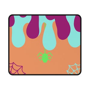 May include: A rectangular mouse pad with a peach-coloured background featuring a dripping pattern in purple and light blue. A small lime green spider hangs from a thread in the centre, with a purple spiderweb in the bottom left and a light blue web in the bottom right corner.