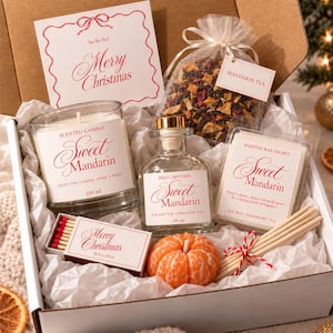 May include: A gift box containing a Sweet Mandarin scented candle, a reed diffuser, a wax sachet, a bag of mandarin tea, a pumpkin-shaped orange candle, and a box of Merry Christmas matches, accompanied by a Merry Christmas card with red text.