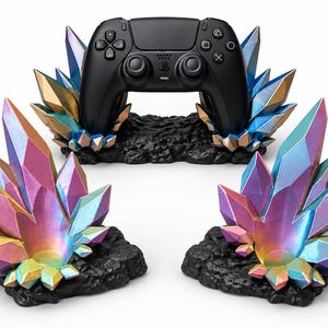May include: A black video game controller rests on a black textured base surrounded by iridescent, multi-colored crystal formations. Two additional matching crystal-themed stands are positioned in the foreground, each featuring a black rocky base.