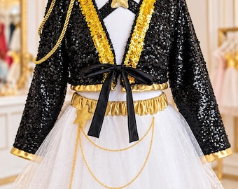 May include: A two-piece outfit featuring a black sequined long-sleeve jacket with gold trim, a black ribbon tie, and a gold star accent. The white skirt has a gold elastic waistband, a gold star, and two draped gold chains across the front.