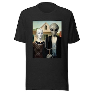 Op de afbeelding: Een antracietgrijs t-shirt met een grafische print van een bleke mensachtige figuur en een grijze alien die voor een huis staan. De alien houdt een drietandige hooivork vast. Het ontwerp is een parodie op American Gothic in een realistische stijl.