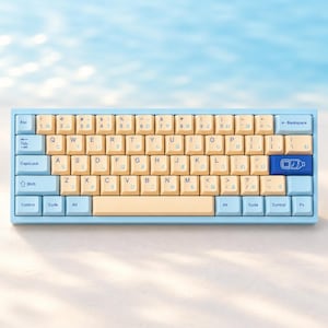 May include: A mechanical keyboard featuring light blue outer keys and beige central keys. The keycaps display both English letters and Japanese hiragana characters. A dark blue enter key features a white line drawing of a water bottle.