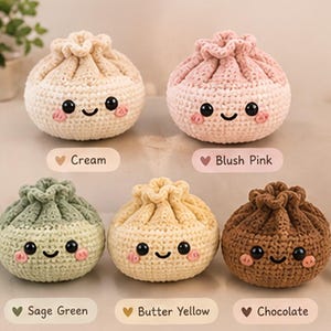 May include: Five round, crocheted plush toys shaped like dumplings, each with black plastic eyes, a stitched smile, and pink cheeks. The colours are labelled as Cream, Blush Pink, Sage Green, Butter Yellow, and Chocolate. The text Colour Variations appears at the top.