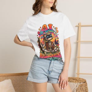 May include: A white t-shirt featuring a colorful graphic of a robot sitting in a lotus position. The robot wears a vest and headband, surrounded by flowers and a rainbow. The text reads AI HALLUCINATING REALITY in bold, multi-colored letters.