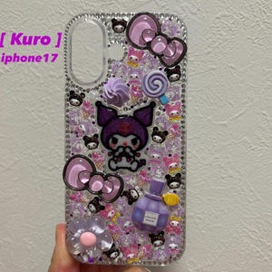Puede incluir: Una funda de teléfono transparente decorada con dijes de resina morados y rosas, incluyendo una figura central morada, lazos, una piruleta y un frasco de perfume. La superficie está cubierta de pequeños brillantes y varios iconos en miniatura.