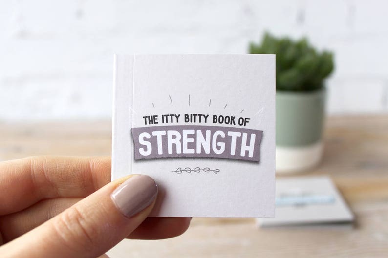 May include: A small white book with the title "The Itty Bitty Book of Strength" printed in black on a gray banner.