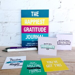 May include: A set of motivational and inspirational journals and cards. The journals are titled "The Happiest Gratitude Journal" and "The Itty Bitty Positivity Book". The cards have phrases like "Have Passion. Take Action. Magic will happen" and "You've Got This".