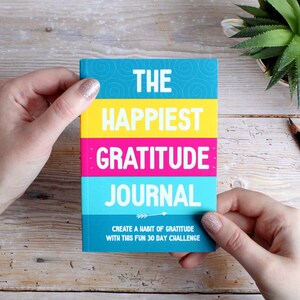 May include: A colourful gratitude journal with the text "The Happiest Gratitude Journal" and "Create a habit of gratitude with this fun 30 day challenge".