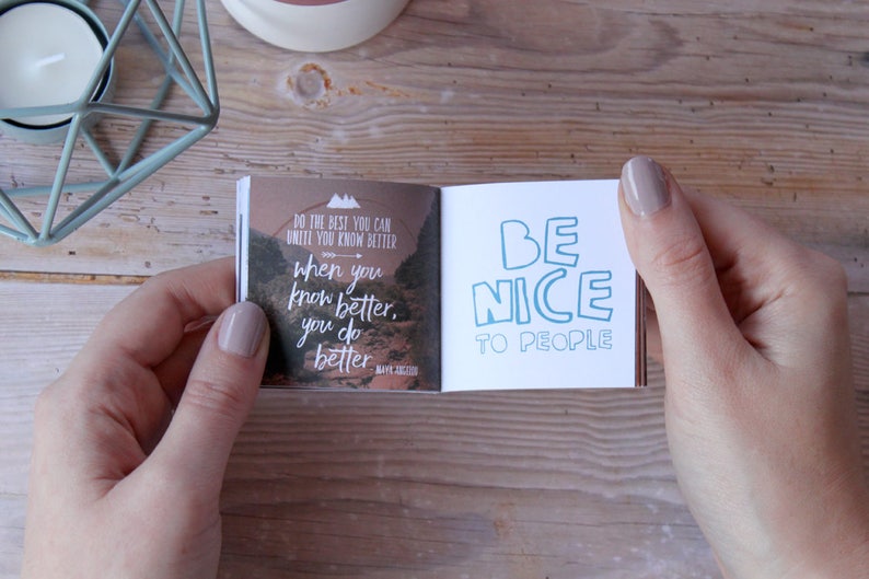 May include: A small, open book with a motivational quote on each page. The left page features a landscape scene with the quote "Do the best you can until you know better, when you know better, you do better." The right page has the quote "Be nice to people" in blue text.