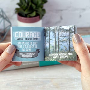May include: A small blue and white book with the text "COURAGE DOESN'T ALWAYS ROAR!" and "SOMETIMES IT'S THE QUIET VOICE AT THE END OF THE DAY SAYING... I WILL TRY AGAIN TOMORROW". The back of the book shows a photo of a forest with the text "GLENVEAGH NATIONAL PARK COUNTY DONEGAL".