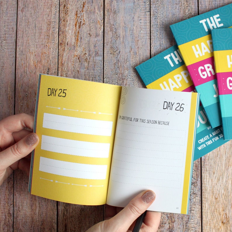 May include: A yellow and white journal with the text "Day 25" and "Day 26" on the pages. The journal is open to a page that says "I'm grateful for this season because".