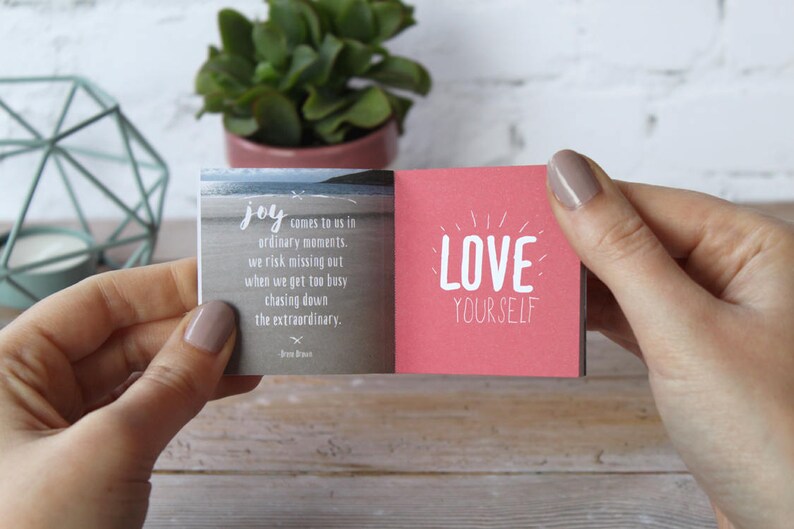 May include: A small pink and gray book with the text "joy comes to us in ordinary moments. we risk missing out when we get too busy chasing down the extraordinary." and "LOVE YOURSELF" on the front and back covers.