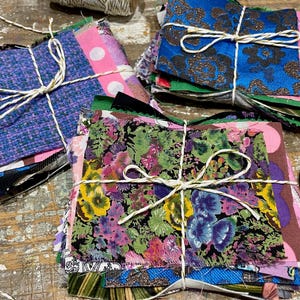 May include: Several bundles of fabric offcuts in diverse patterns and colours, secured with twine. The fabrics feature floral, polka dot, and textured designs. A pair of black scissors is visible.