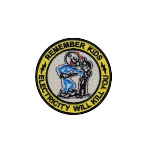 May include: A circular embroidered patch with a yellow border featuring the black text REMEMBER KIDS ELECTRICITY WILL KILL YOU. The center shows a cartoon character in a blue suit interacting with a figure on a light gray background.