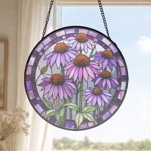 Può includere: Un acchiappasole circolare in vetro colorato raffigurante un gruppo di fiori di echinacea viola con centri arancioni. I fiori presentano petali viola chiaro e steli verdi, racchiusi in una cornice di metallo scuro e appesi a una catena nera.