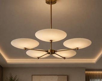 Puede incluir: Una lámpara de araña de cinco luces con una varilla central y estructura de metal en tono latón, con cinco pantallas circulares de vidrio blanco esmerilado dispuestas horizontalmente. La lámpara emite un brillo suave y cálido desde cada disco.