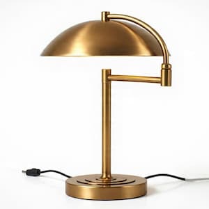 May include: A brass-toned metal table lamp featuring a dome-shaped shade, a vertical central post, and an adjustable horizontal arm. The lamp has a circular base with concentric ring detailing and includes a black power cord extending outward.