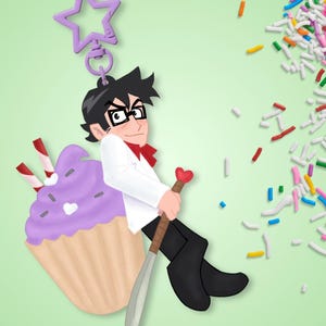 Op de afbeelding: Een sleutelhanger met een personage met zwart haar en een bril, gekleed in een wit jasje en een zwarte broek, die een zwaard met een hartvormige knop vasthoudt, naast een paarse cupcake met twee gestreepte rietjes.